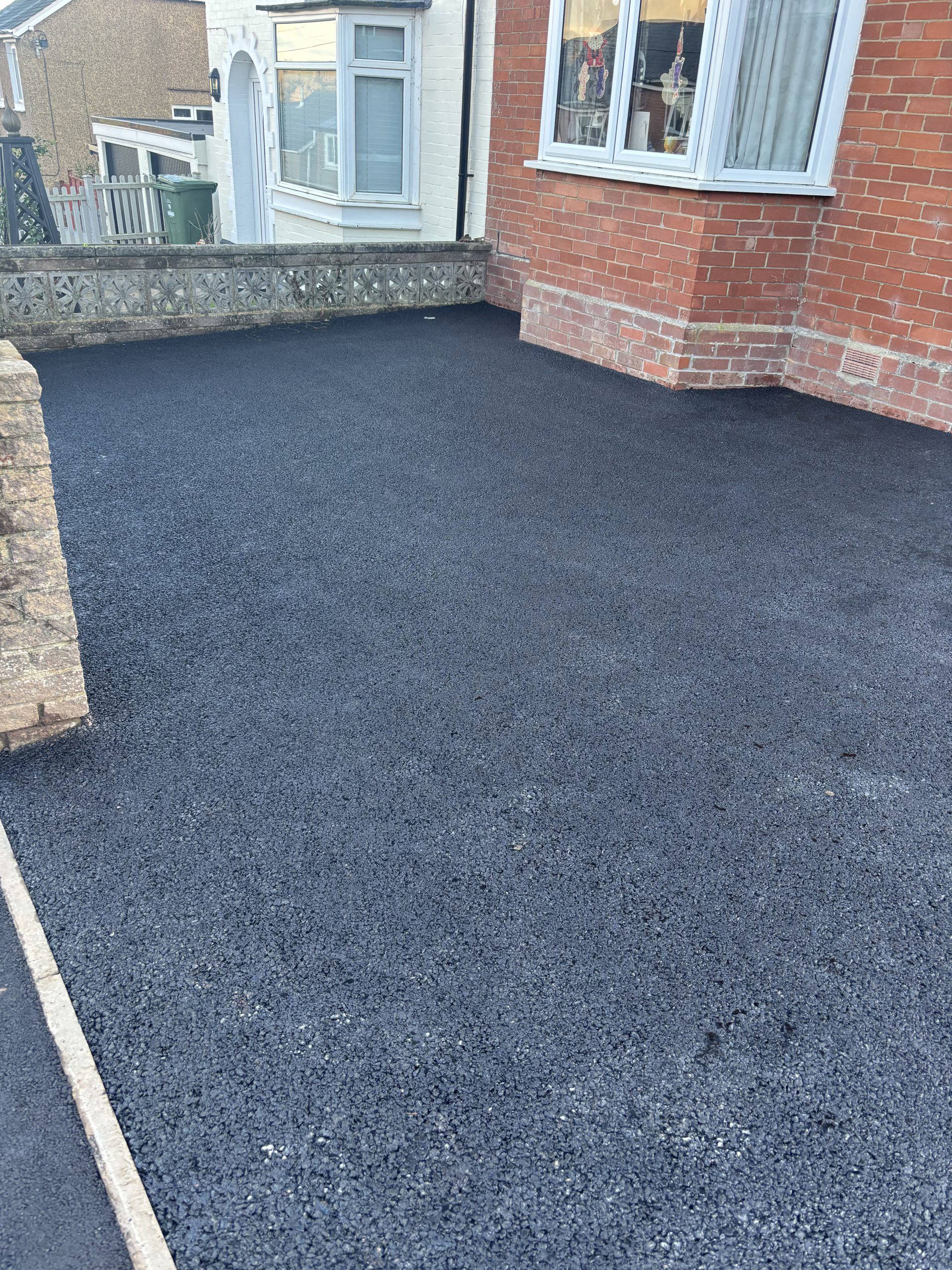 Completed black tarmac driveway in front of a brick house